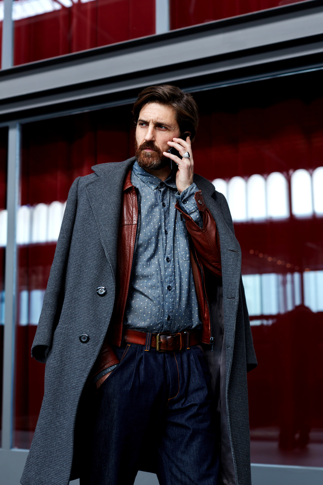 Portrait os stylish fashionable man in elegant coat having phone conversation walking in beautiful hotel hall