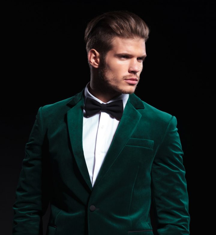 side view of a young elegant man in green velvet suit , he looks away from the camera and stands with hands in pockets